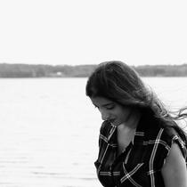Side profile of woman looking down with water behind and air blowing her hair back